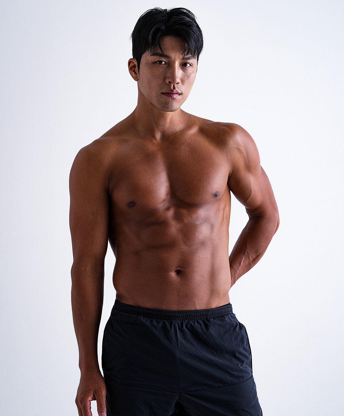 Male model posing shirtless against white background.